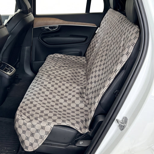 A car seat cover with a beige and black repeating monogram pattern installed on the rear seat of a vehicle.