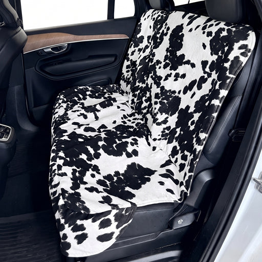 A car seat cover with a black and white cow print pattern installed on a vehicle's front seat, shown inside a car interior.