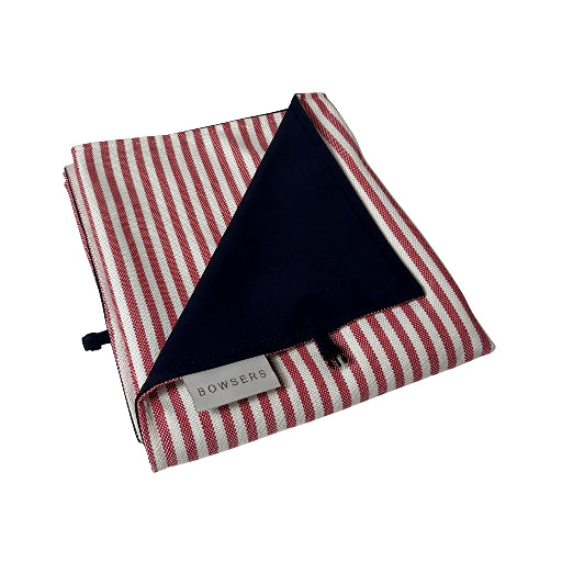 A folded striped fabric accessory with red and off-white vertical stripes on the exterior and a solid dark navy interior, featuring a small white label that reads BOWSERS.