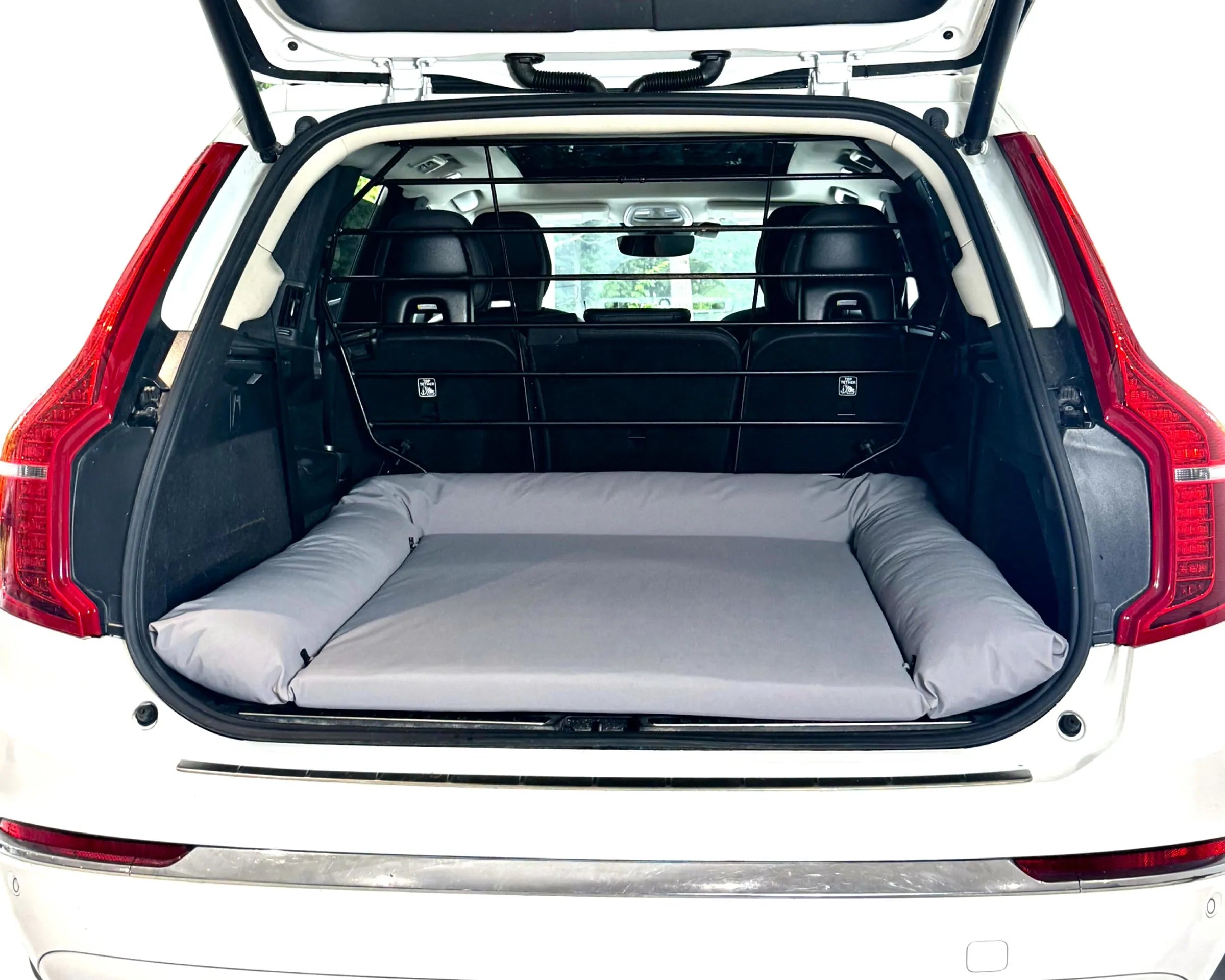 A gray inflatable camping bed or sleeping pad displayed inside the open trunk of a white SUV, showing its padded sides and flat floor.