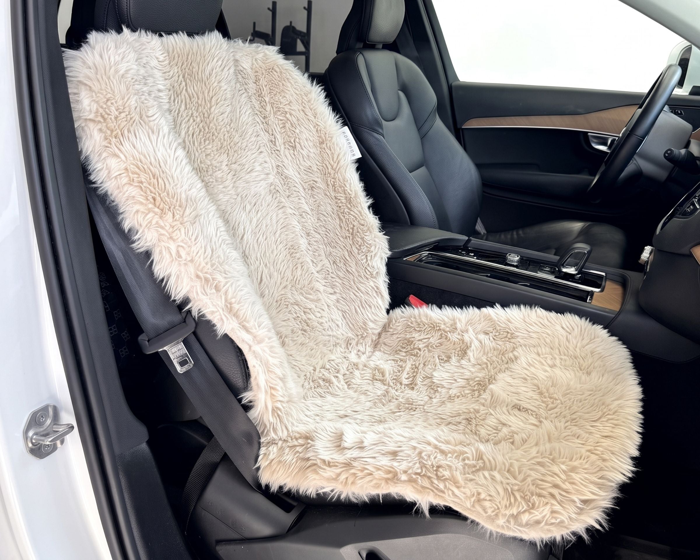 Bowsers Single Bucket Seat Cover  A fluffy faux-fur car seat cover in a light beige/cream color, shown installed on a black car seat inside a vehicle.