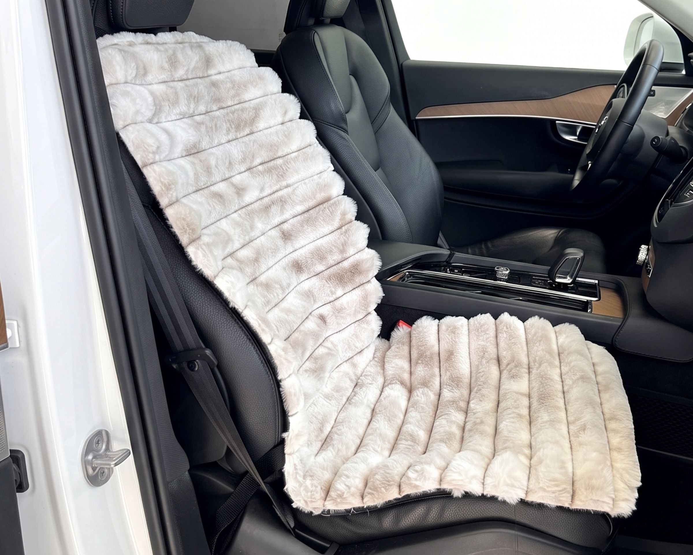 Bowsers Single Bucket Seat Cover.  A plush faux fur car seat cushion set in cream and light brown, shown installed on the front driver's seat and backrest of a black car interior.