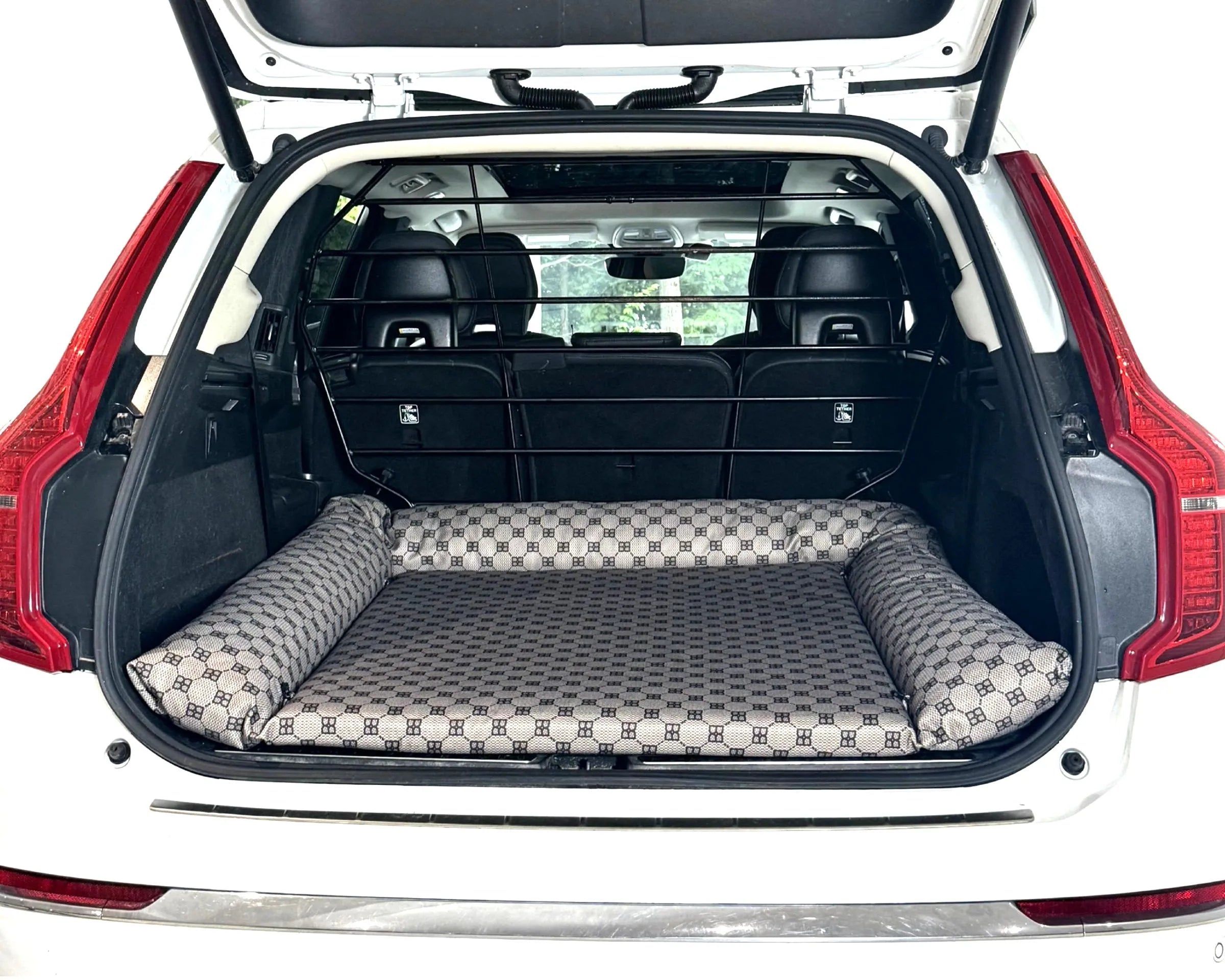 Bowsers SUV Cargo Lounger Dog Bed A pet car bed with a gray and white checkered pattern and raised bolster sides, shown installed inside the open trunk of a white vehicle.